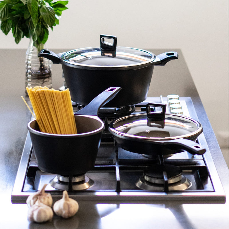 Batería de ollas y sartén Simplit sobre la cocina, con albahaca y pasta
